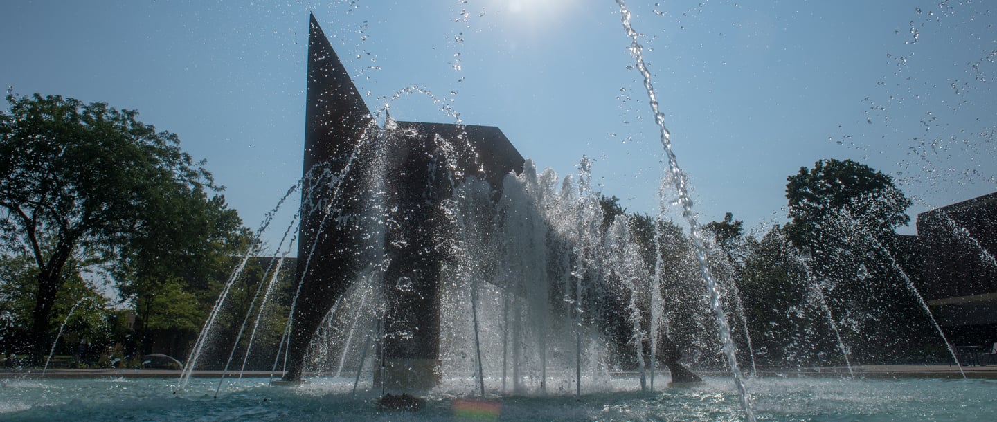 A close-up view of the fountain. The water is splashing and the sun shines above the fountain, creating a rainbow toward the bottom of the shot.
